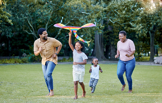 Black family, kite and outdoor fun with parents and children having fun and playing outside at a park in nature. Energy, love and running while being active and bonding with man, woman and kids