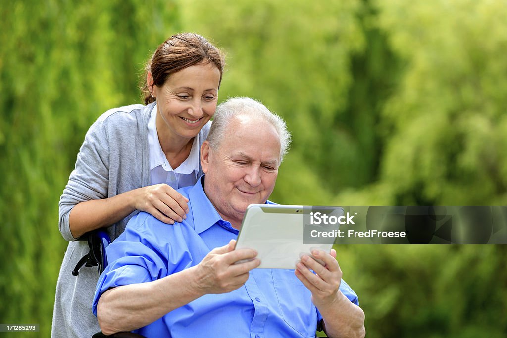 Uomo anziano seduto su una sedia a rotelle con il caregiver - Foto stock royalty-free di Assistente domiciliare