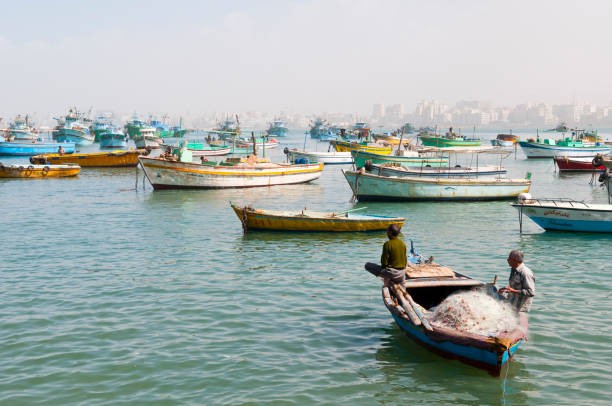 Alexandria, Egypt - February 28, 2008: Two fishermen sit on their small vessel, one tending the fishing net, in  historic Alexandria.