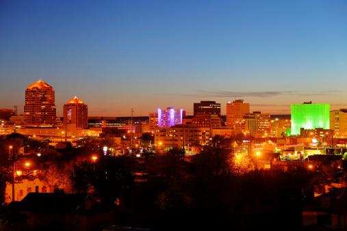 Downtown Albuquerque skyline at dusk. Albuquerque nighttime cityscape illuminated in vibrant colors such as green and blue. Albuquerque is the largest city in the state of New Mexico, United States. Albuquerque is known for its pleasant scenery, southwestern cuisine and International Balloon Fiesta. 