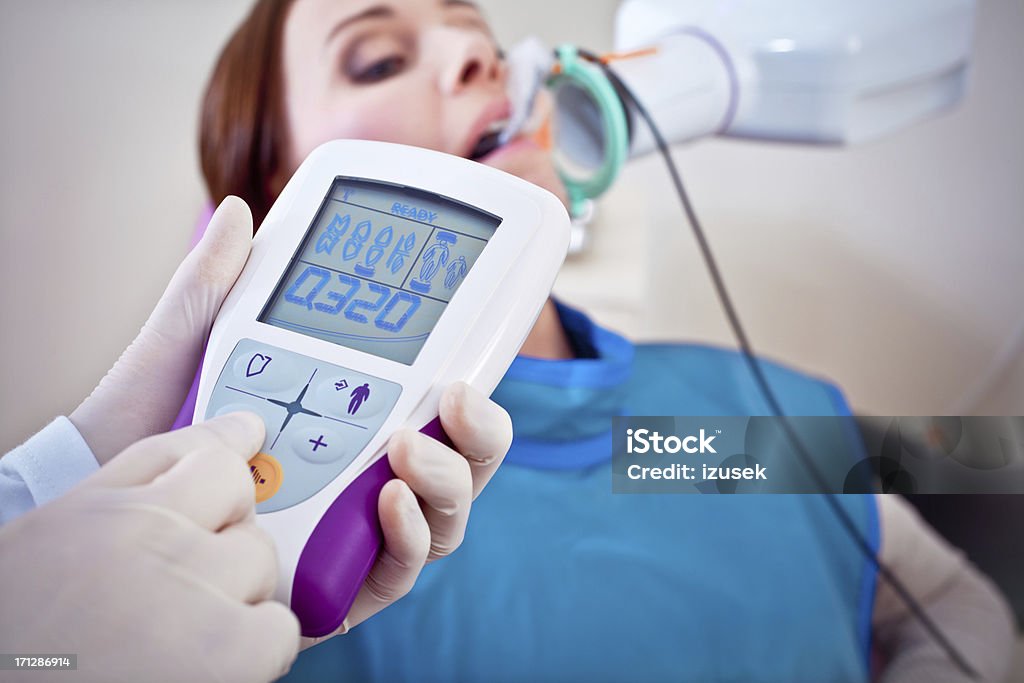 Dentist Taking X-rays of Patient A dentist operates an x-ray machine while her patient sits with protective covering and x-ray film in mouth. Close up on x-ray controls. 30-34 Years Stock Photo