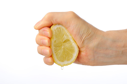 Close-up shot of hand squeezing a lemon isolated on white background.
