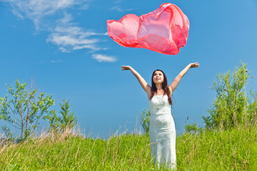 Portrait of pretty woman throwing scarf from her hands in the meadow under blue sky