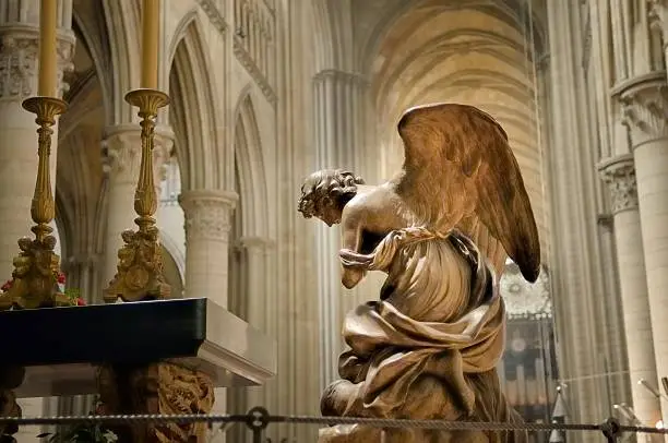 A worshipping angel, or archangel, depending on which one this is, kneels toward the altar in the Notre Dame Cathedral in Rouen. Brass candlesticks are adorned with cherubs or seraphim, depending on your taste