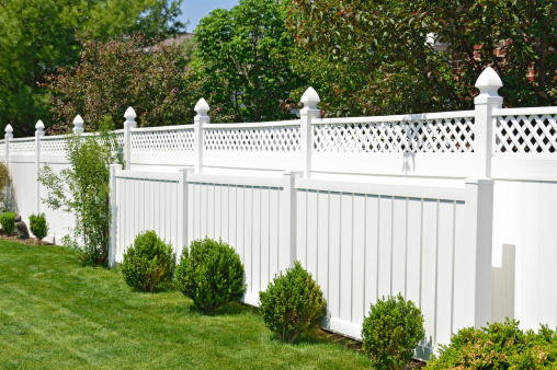 Beautiful white vinyl fence in well manicured back yard surrounded by nice landscaping and trees