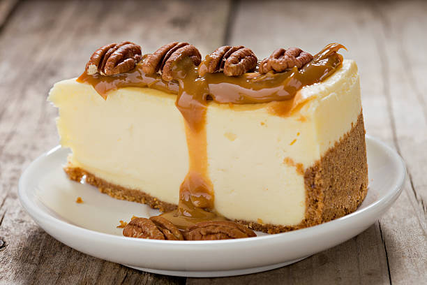 Cheesecake with Caramel And Pecans. An extreme close up side view of a slice of cheesecake covered with gooey caramel and toped with pecan nuts.Shot on a grungy old wooden background. dulce de leche stock pictures, royalty-free photos & images