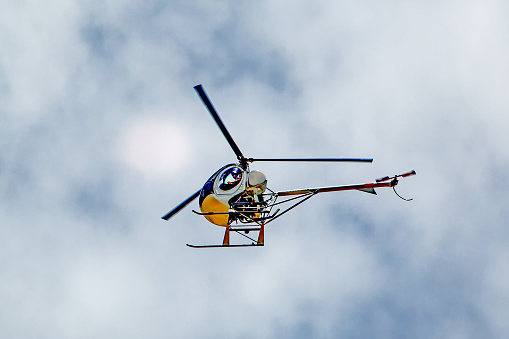 Small two-man helicopter flying overhead with cloudy sky in background