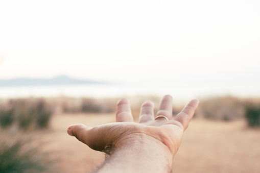 Pov of man hand against a moody scenic destination travel background with bright clear sky and island. Concept of journey and adventure lifestyle people. Dreaming and hope. Open hand palm viewed eyes