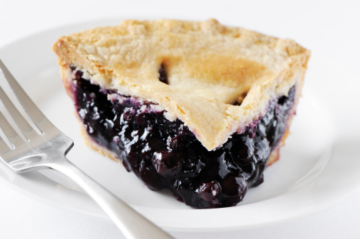 Serving or slice of blueberry pie in a white plate with a fork on a white background.