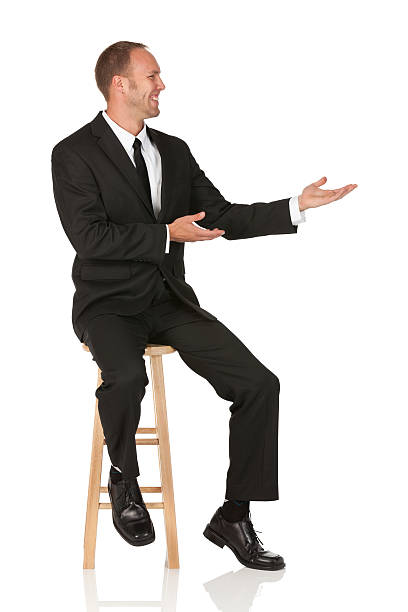 Happy young businessman sitting on a stool and gesturing