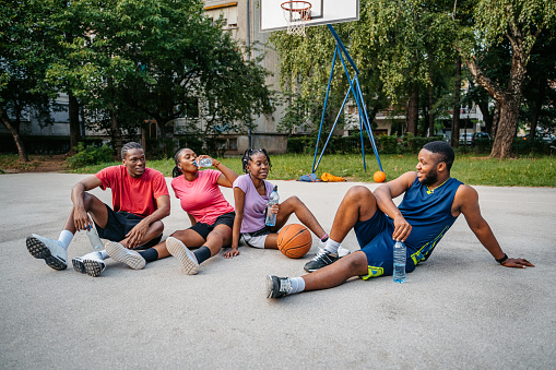 Young black family sitting on the basketball court outdoors,chatting and drinking water after a basketball game.