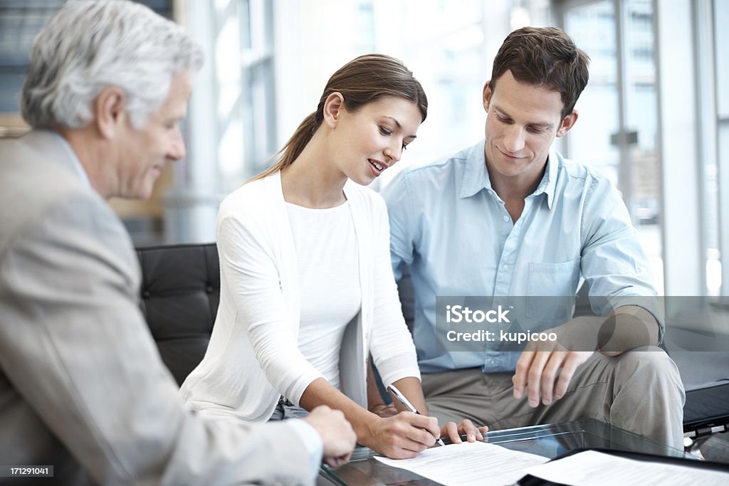 Making the right decisions to protect their future A young couple signing the paperwork for their new investments Couple - Relationship Stock Photo