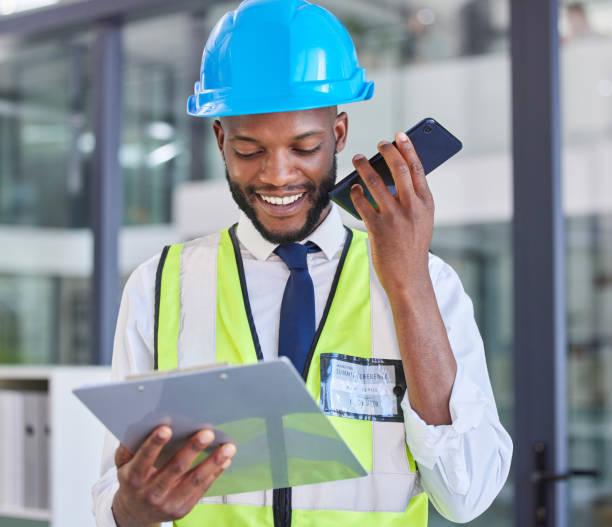 istock Construction worker, clipboard and phone with a man on a wifi call in a engineering office. Architecture, contractor and african American man reading list while on a phone call for industry 1712915524