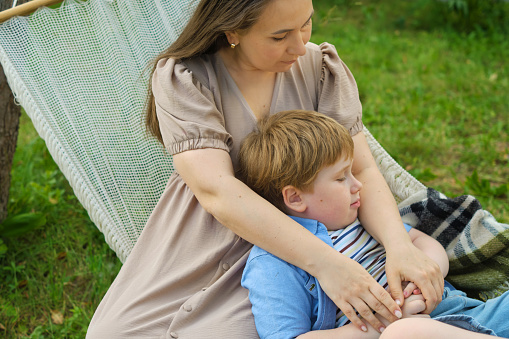 tender moment unfolds as a loving mother and her 5-year-old son engage in heartwarming dialogue, all while nestled in a hammock on a balmy summer day.