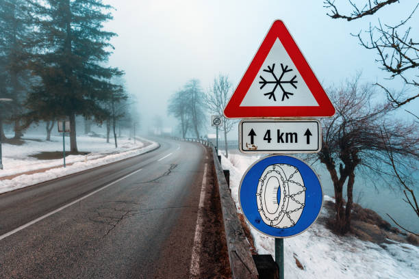 Beware of Ice or snow triangular warning sign and Chains required in winter traffic sign by the road, selective focus