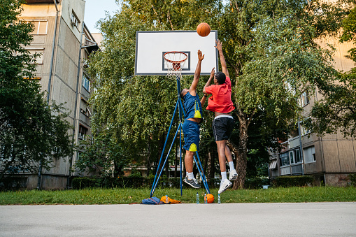 Two young black men playing basketball on a basketball court outdoors.