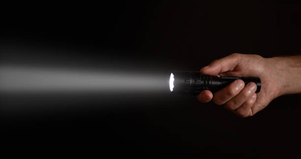 Male hand holding a led flashlight with a wide white beam on a black background, leaving the right side of the frame Male hand holding a led flashlight with a wide white beam on a black background, leaving the right side of the frame. flashlight stock pictures, royalty-free photos & images