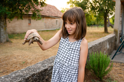 A happy girl is holding a turtle animal in the yard