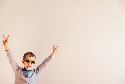 Child with funny sunglasses raising arms excited in victory sign.