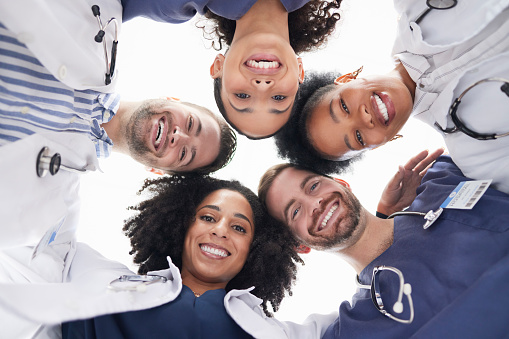 Happy people, portrait and doctors in huddle, teamwork or unity in healthcare mission together below. Low angle of excited group of medical professionals smile in team building, support or goals