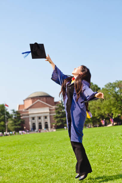young woman jumping in her graduation and throwing hat at university campus
