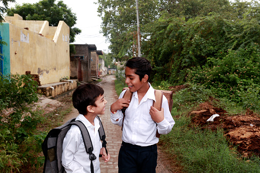 Two primary or high school student wearing school uniform discussing something face to face after school vacation in street also carrying school bag