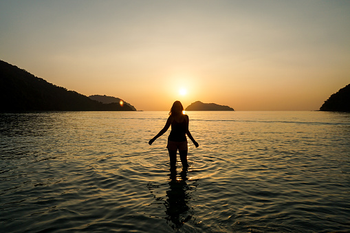 Silhouette of a woman looking the sunset at the beach. An entrancing image of a woman on a beach, her silhouette glowing with a summer rim light.