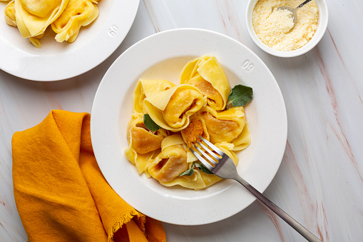 Tortelloni or tortelli di zucca, italian pasta stuffed with pumpkin,  Ravioli served with butter and sage, parmesan cheese. Directly above.
