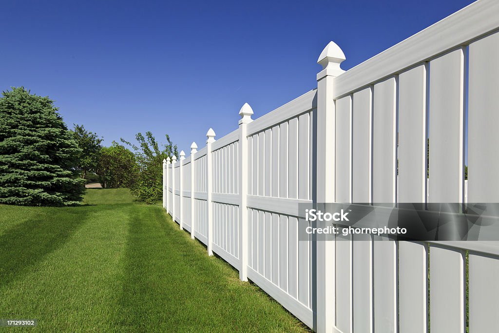 New white fence New and contemporary white vinyl fence running across a nicely landscaped backyard with lawn and blue sky in the background. Fence Stock Photo