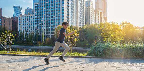 a boy runs along the road in a city park. a child is jogging on a sunny day outside in a metropolis
