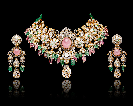 A beautiful golden Necklace and Earrings with green emerald stones, ruby, and diamonds, on a black background.
