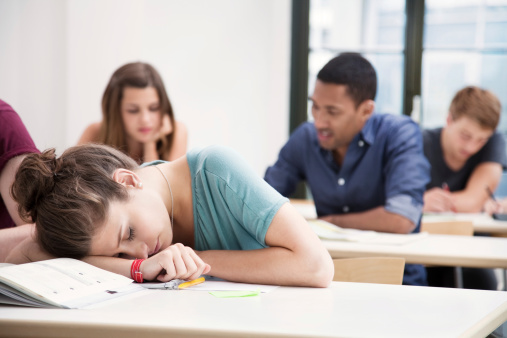 Photo of female student sleeping in class. Shallow depth of field, multi-ethnic group of students in the background.