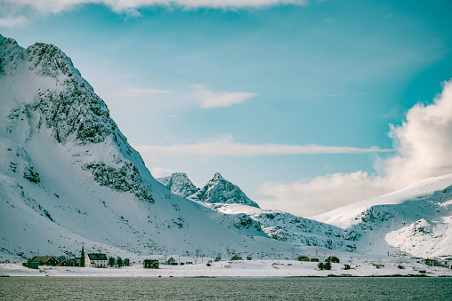 Sonwy winter landscape with the village of Flakstad at the shore of Flakstadoya one of the islands of the Lofoten archipel in Norway The mountains are covered in snow and the village church of Flakstad lies below the mountains.