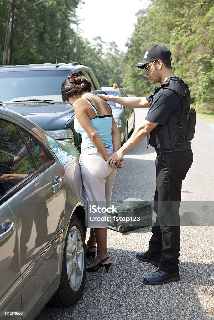 Policeman putting un pie atado al suelo a mujer junto a los vehículos - Foto de stock de Detención libre de derechos