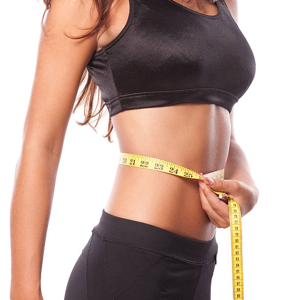 Beautiful woman is measuring her waist A beautiful tanned and fit woman is measuring her waist. exercising tape measure women healthy lifestyle stock pictures, royalty-free photos & images