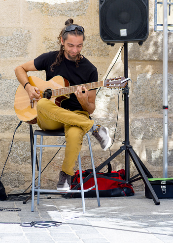 man sitting on a stool in an outdoor setting, playing an acoustic guitar