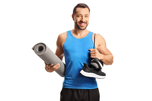 Man in sportswear holding an exercise mat and a pair of sneakers isolated on white background