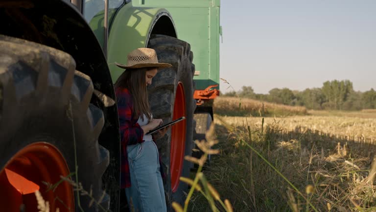 SLO MO Female Agronomist in Sunhat Using Digital Tablet while Leaning on Tractor on Corn Field during Sunny Day