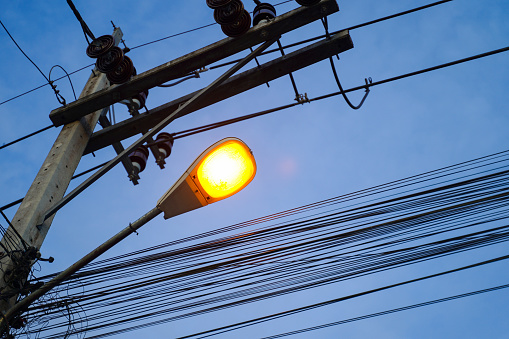 Lighting lamp hanging on electricity pole with many cables in the evening.