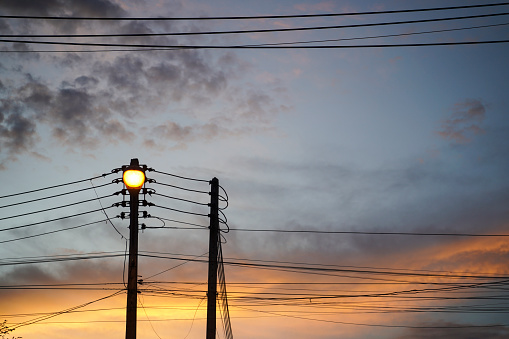 Lighting lamp hanging on electricity pole with many cables in the evening.