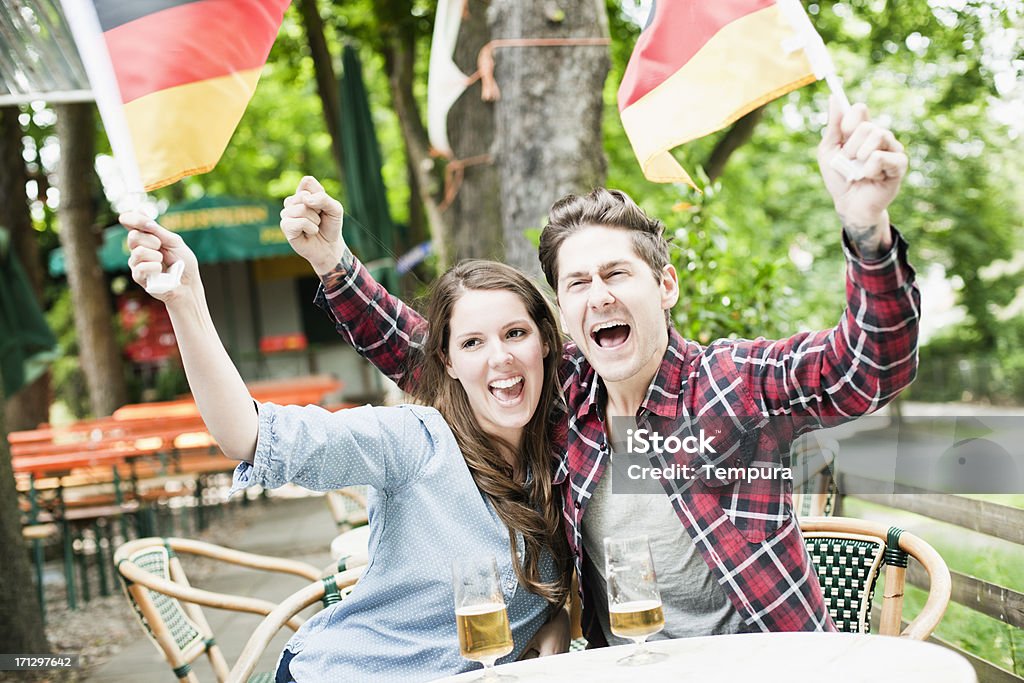 Couple celebrating Germany's sports victory at a country pub. Two young Germans cheering their team while sharing a drink at a bar. Made in Berlin during 2012's Lypse. Arms Raised Stock Photo