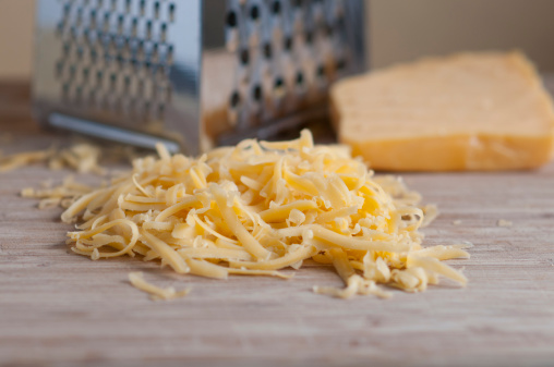 Grated cheddar cheese on wooden board with cheese grater and a block of cheese in the backgroound.  Focus is on the grated cheese.  Selective FocusTo see more of my food images click on the link below: