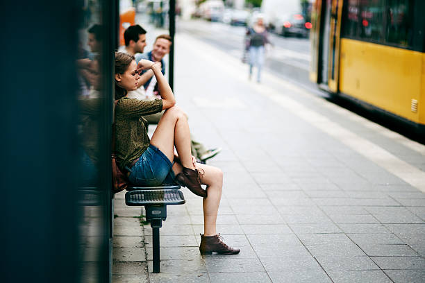 Portrait of a worried young woman sitting on a tram stop in Berlin. Very shallow depth of field, blurred people and yellow tram in the background.