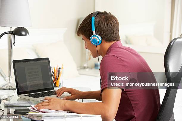 Teenage Boy Studying At Desk In Bedroom Wearing Headphones Stock Photo - Download Image Now