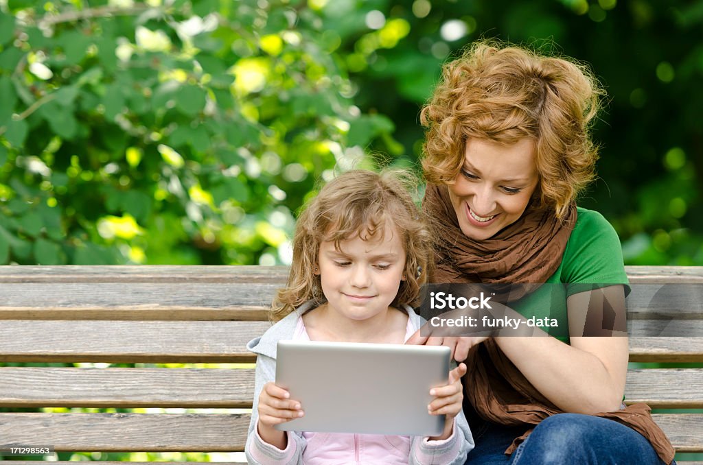 Young mother and child A young mother is showing her daughter something on the touchscreen device in a park. Adult Stock Photo