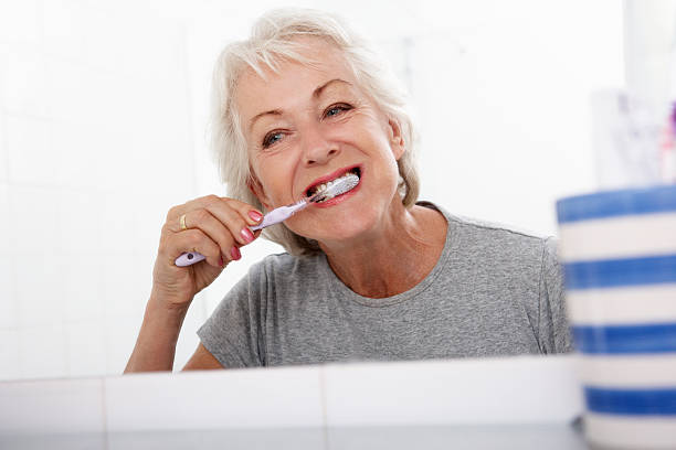 старший женщина, чистить зубы в ванной комнате - dental hygiene human teeth toothbrush brushing teeth стоковые фото и изображения