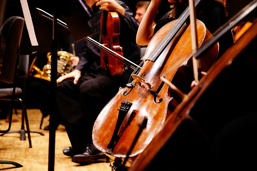 Musician rests his cello on stage surrounded by the rest of the symphony orchestra.