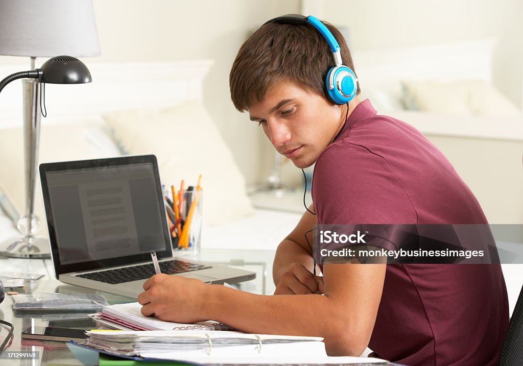 Adolescente ragazzo studiare alla scrivania In camera da letto con le cuffie - Foto stock royalty-free di Computer portatile