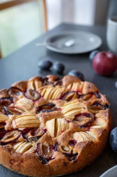 Delicious autumn and winter cake with fresh baked apple plum cake. Served whole and ready to eat on a table at home. Closeup