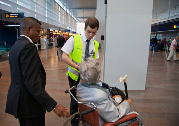 Senior woman in wheelchair getting help from airline representatives. "Stockholm, Sweden - June 28, 2012:Arlanda airport.  Senior woman in wheelchair getting help from airline representatives. The woman holding a walking stick is looking up at a porter while another representative is watching. People moving in the background in the departure hall. Multiethnic." airport porter stock pictures, royalty-free photos & images